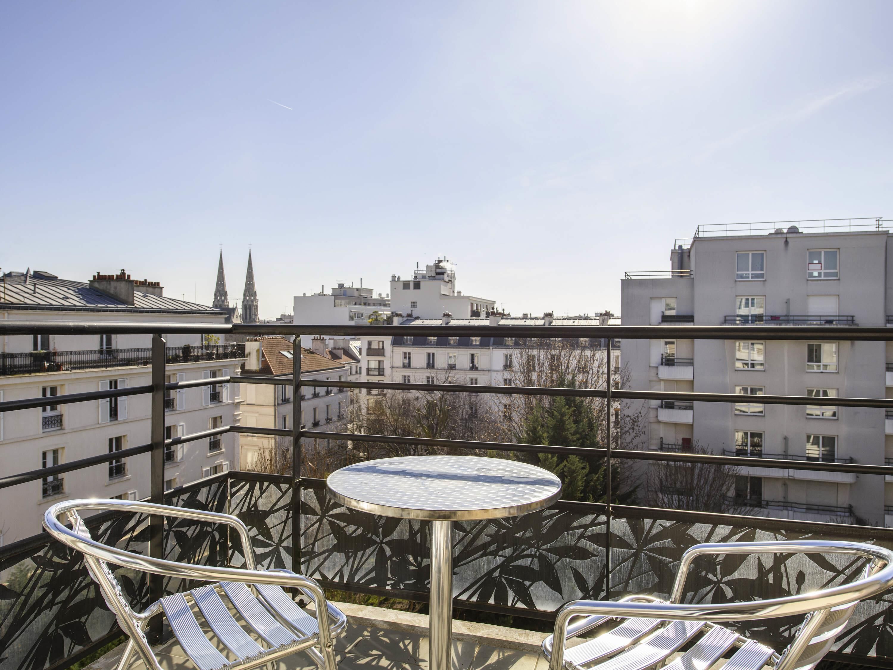 A balcony with a round table and two chairs, overlooking a cityscape with buildings and a church spire.