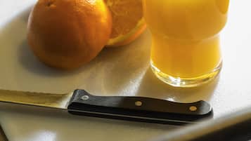 A glass of orange juice, a knife, and oranges on a cutting board.