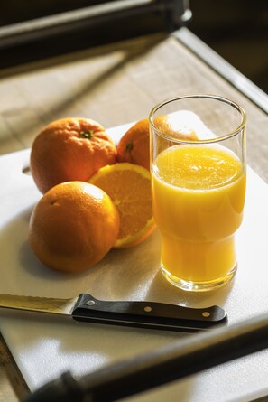 A glass of orange juice, a knife, and oranges on a cutting board.