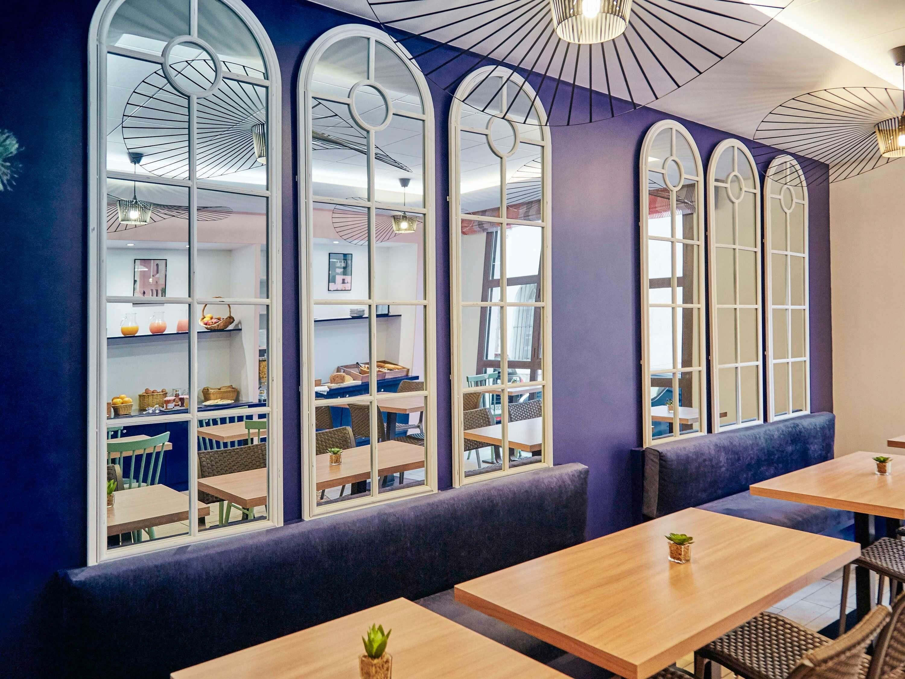 Een restaurant met grote gewelfde ramen, houten tafels en zachte zitplaatsen.