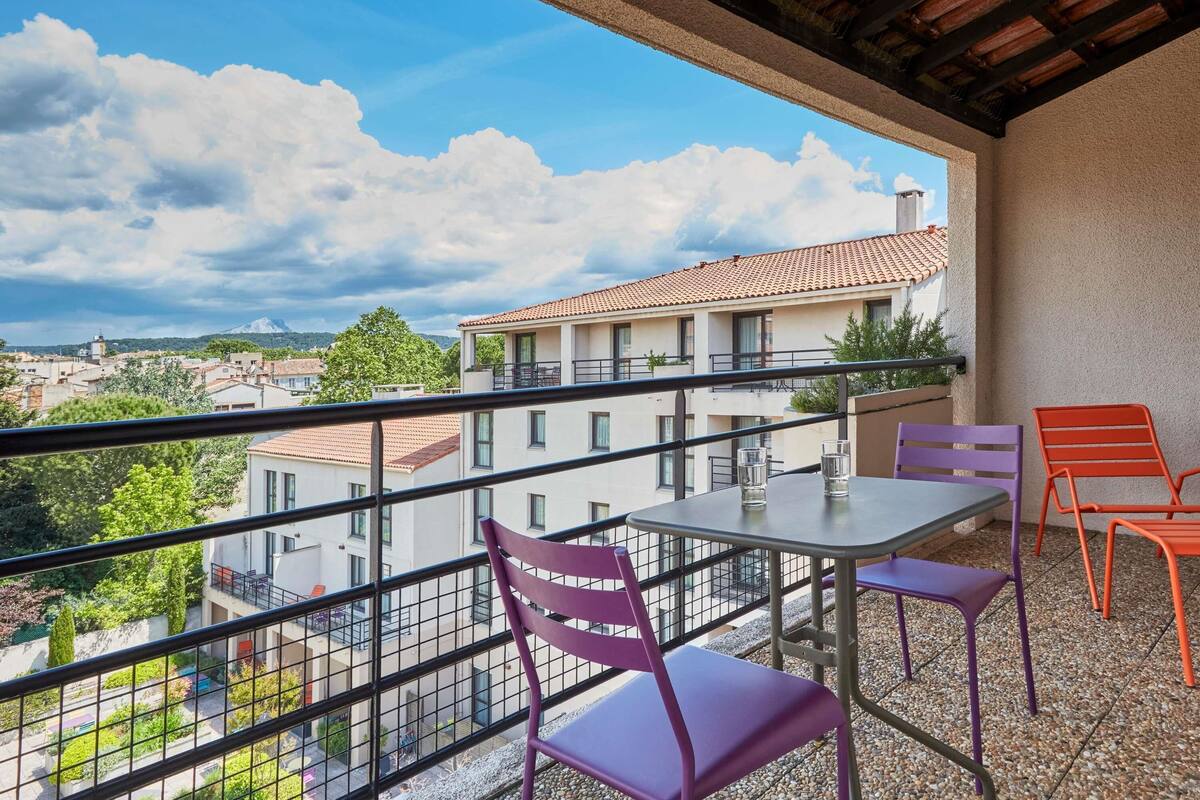 A balcony with a table and chairs, overlooking a residential area with buildings and trees.