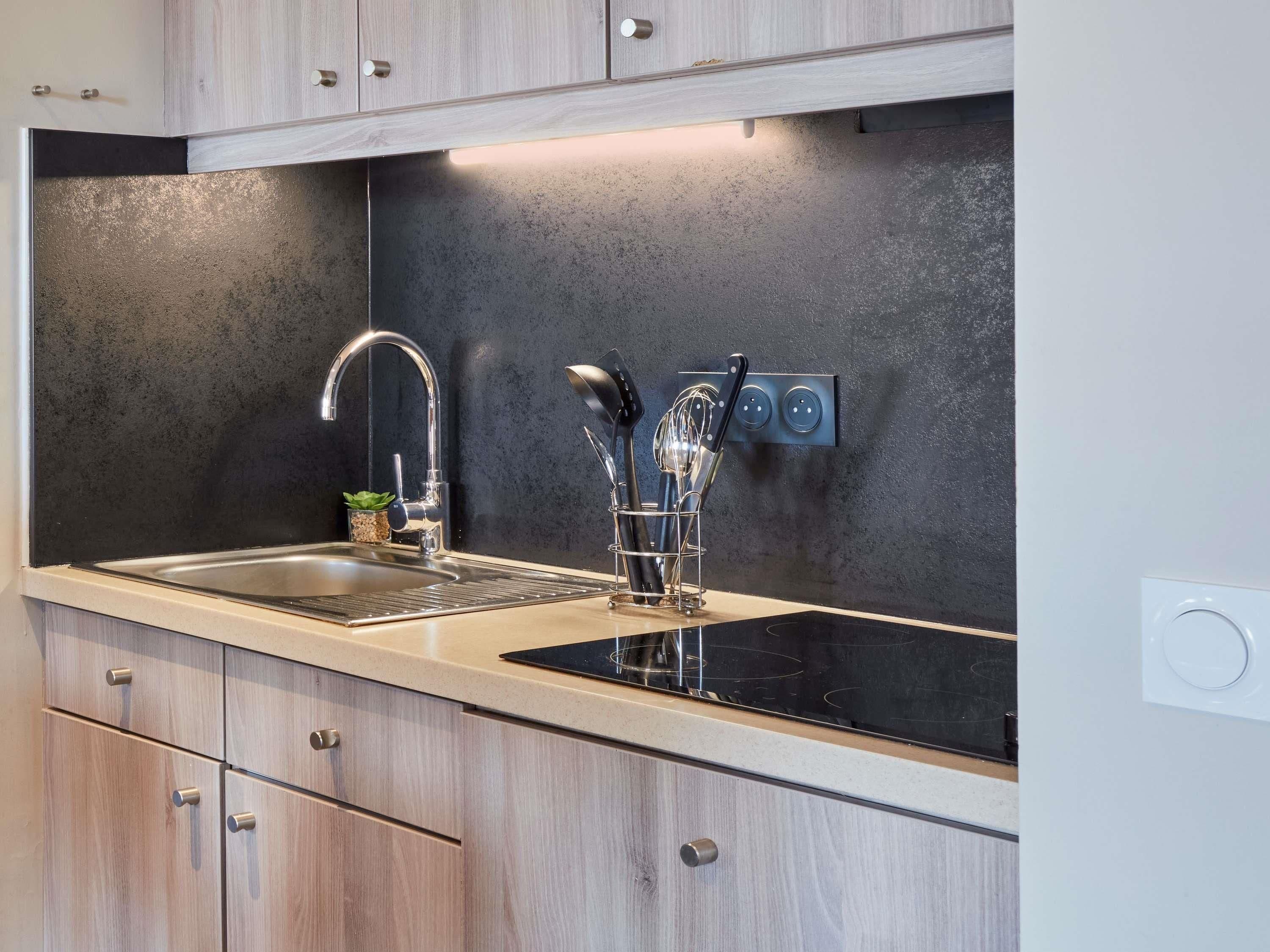 A kitchen with a stainless steel sink, wooden cabinets, a black countertop, and a wall-mounted knife holder.