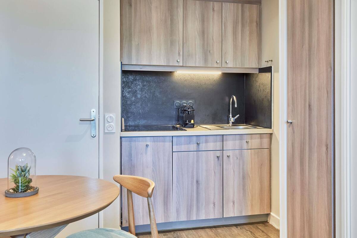 A compact kitchen with wooden cabinets, a built-in sink, and a coffee machine.