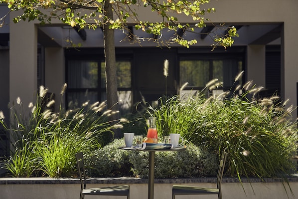 An outdoor dining area with a table set for two, featuring a glass of orange juice, two cups, and a bottle.
