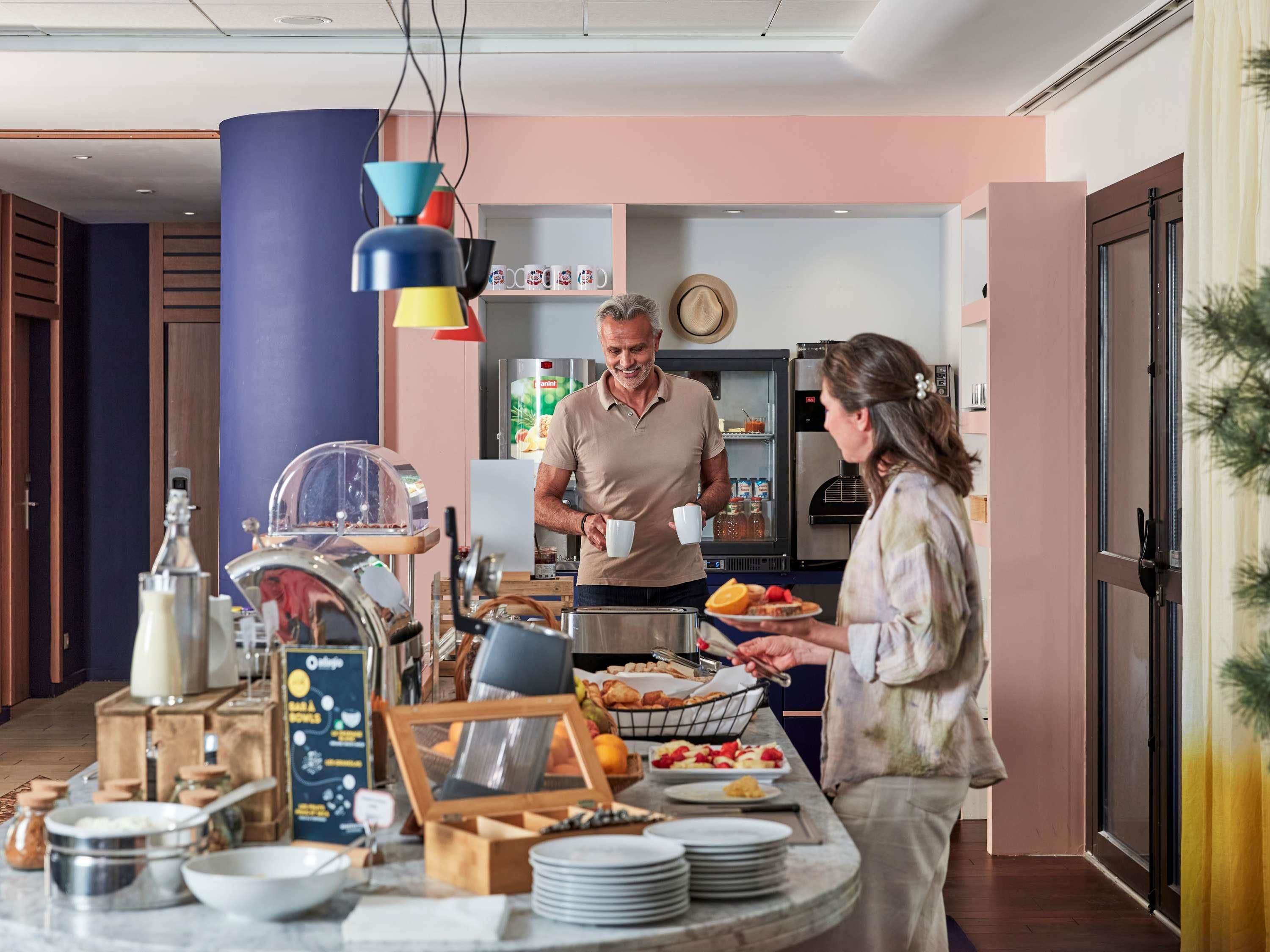 A breakfast buffet with a variety of food items, a coffee machine, and a refrigerator in the background.
