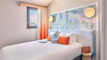 Una habitación de hotel con cama, ventana con cortinas, un cuadro en la pared y una mesita de noche.