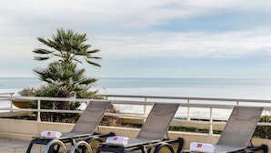 Tres tumbonas con toallas, una palmera y vista al mar.