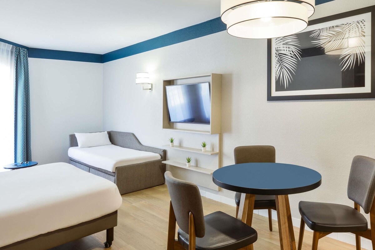 Une chambre d’hôtel avec un lit, un bureau, une chaise, une télévision et un tableau encadré au mur.