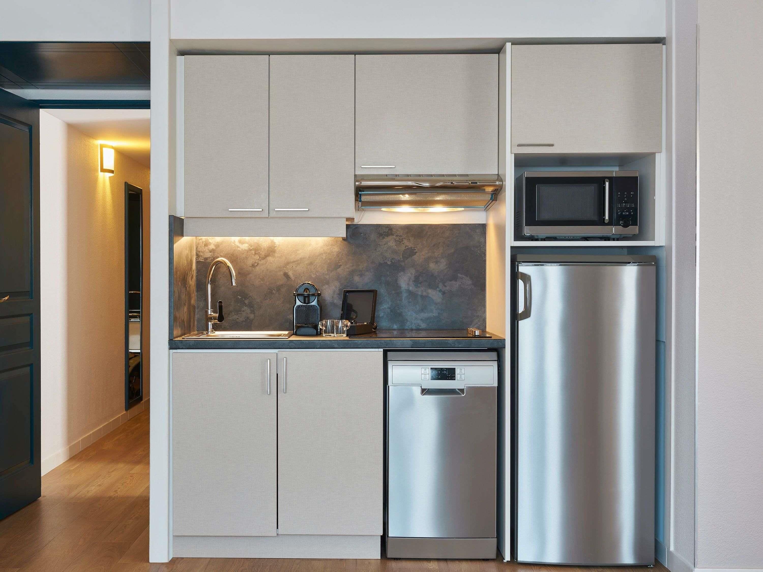 A compact kitchen with a built-in microwave, a stainless steel refrigerator, a dishwasher, and a coffee maker.