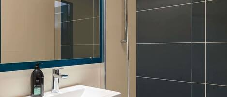 A modern bathroom with a white sink, a mirror with a blue frame, and a shower with a glass door.