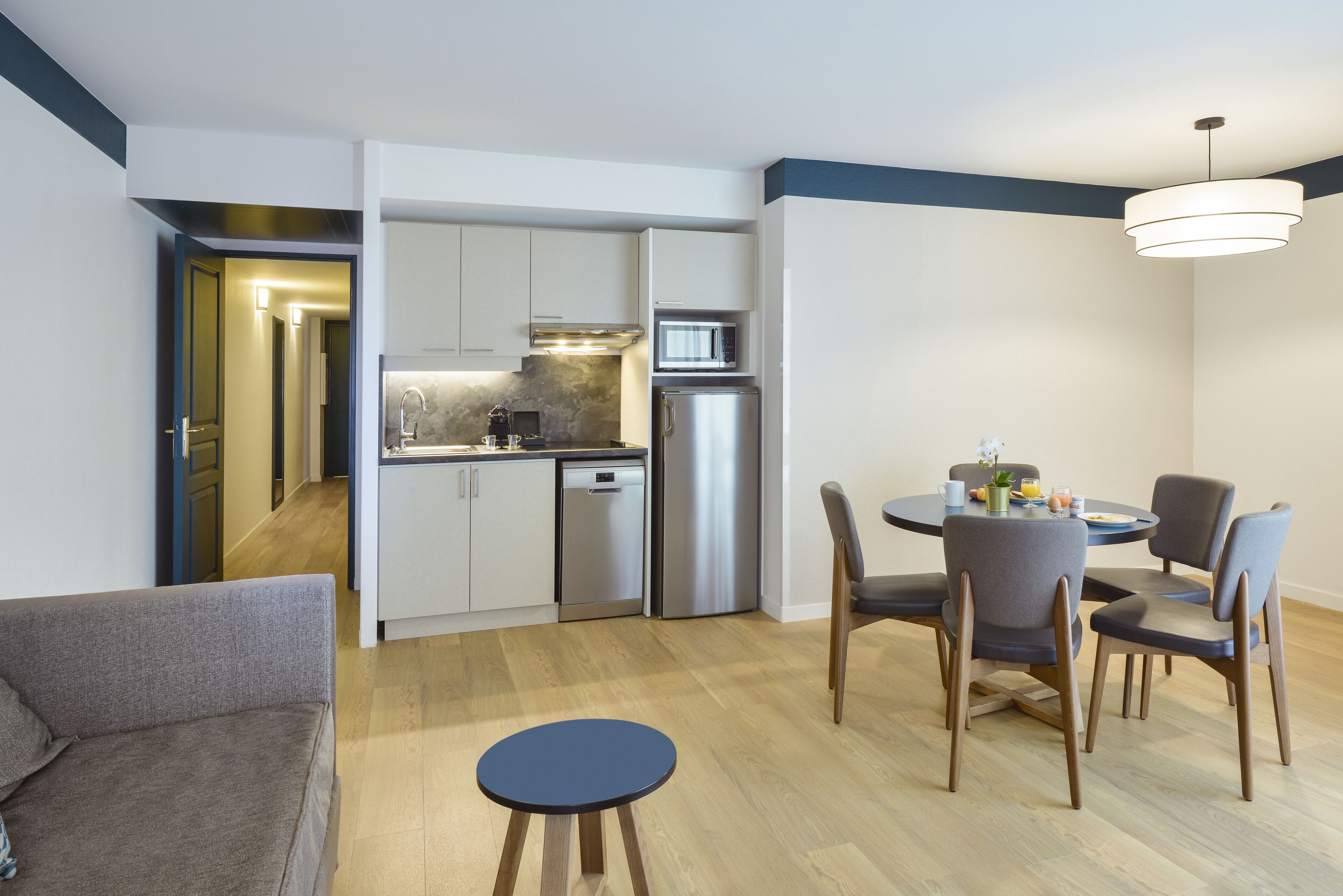 A compact kitchen with modern appliances, a dining area with a round table and chairs, and a sofa in the living area.