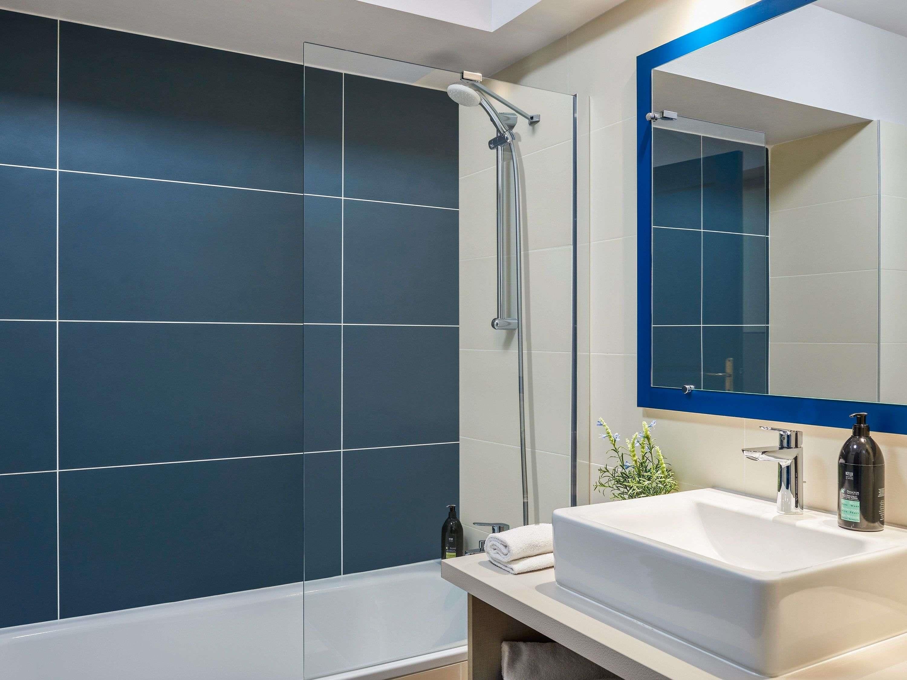 Une salle de bain moderne avec une douche à parois de verre, un lavabo blanc et un grand miroir doté d’un cadre bleu.