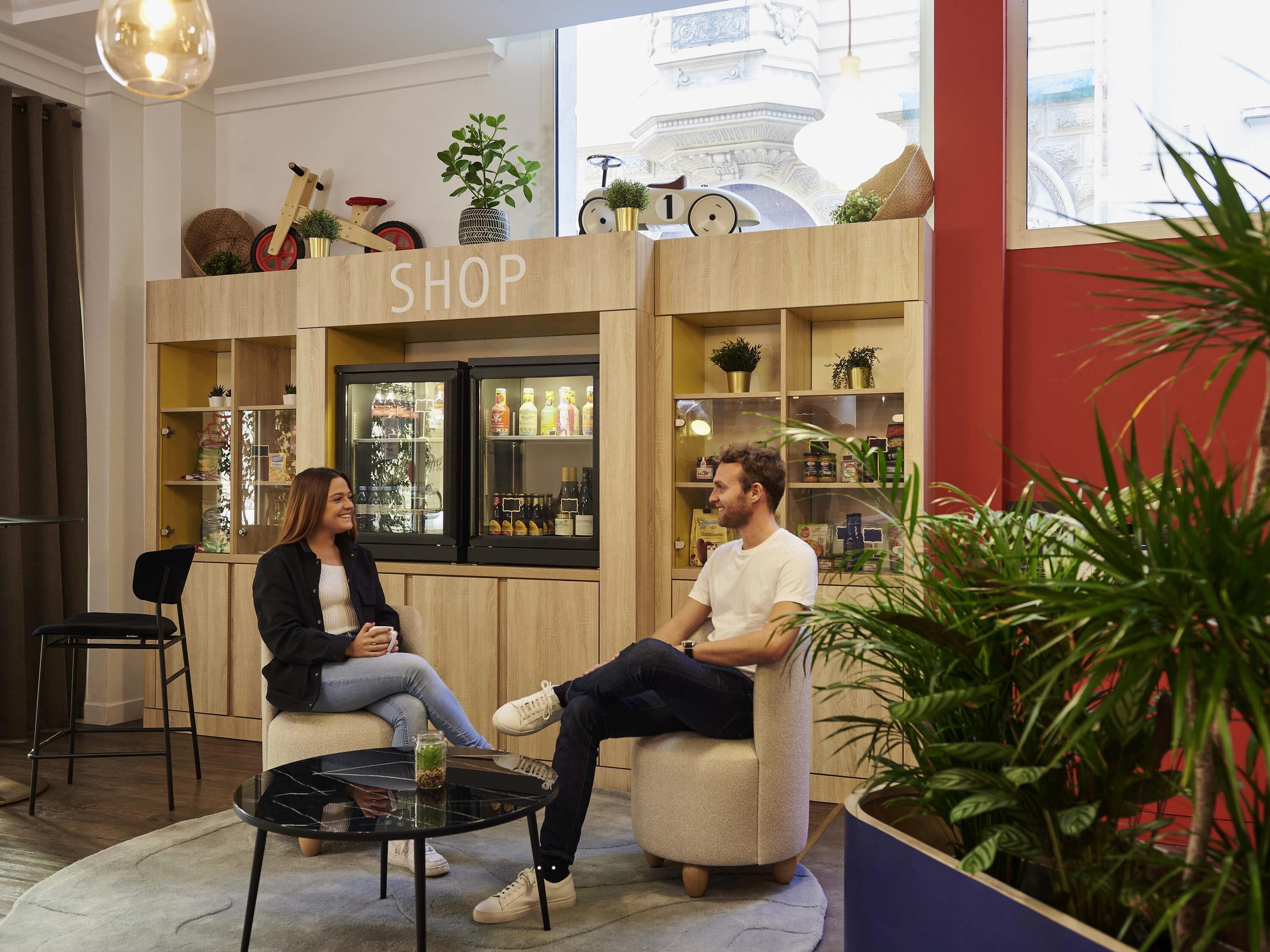 Two people seated in a modern lounge area with a shop in the background.