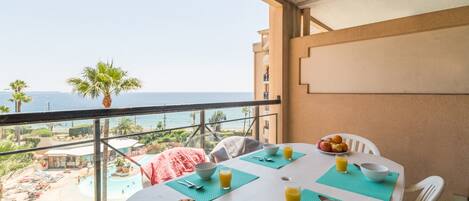 A balcony table with breakfast items, a view of the beach, and a palm tree.