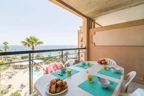 Une table sur le balcon avec des aliments pour le petit-déjeuner, une vue sur la plage et un palmier.