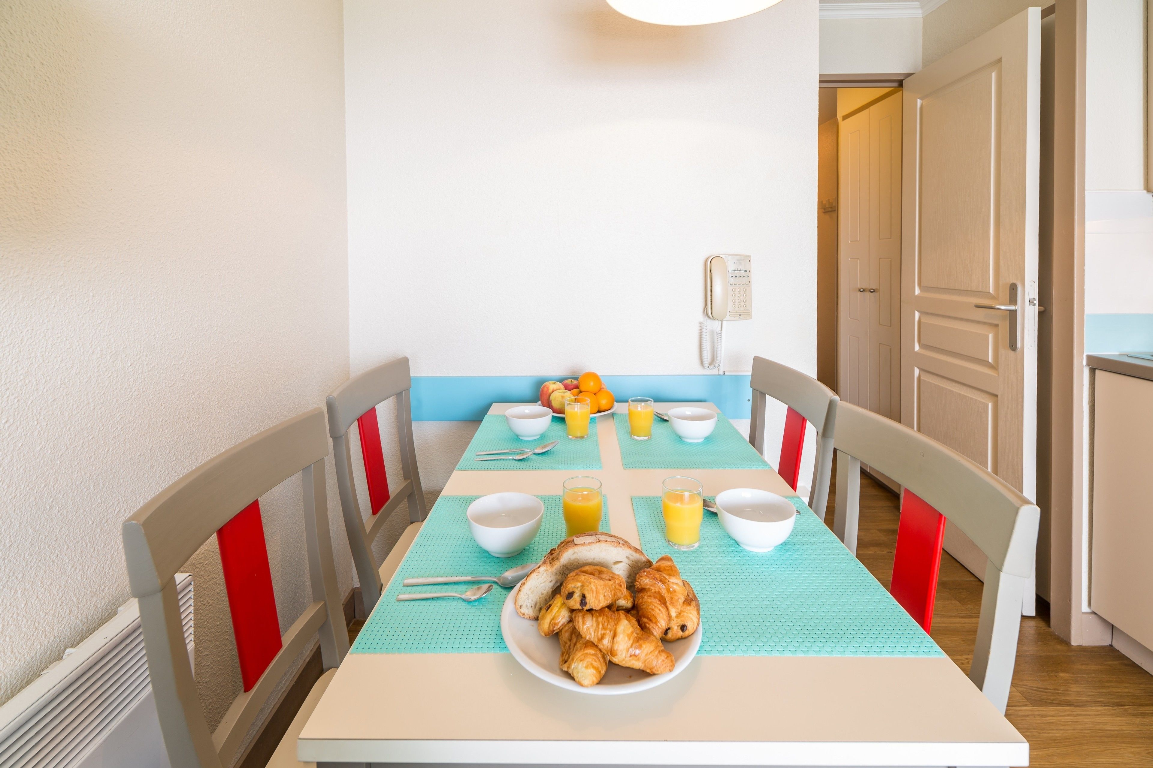 A dining table with breakfast items, chairs, and a telephone on the wall.