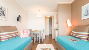 Ein gemütliches Zimmer mit zwei türkisfarbenen Sofas, gestreiften Kissen, einem kleinen Tisch mit einer Kerze und einem gerahmten Bild an der Wand.