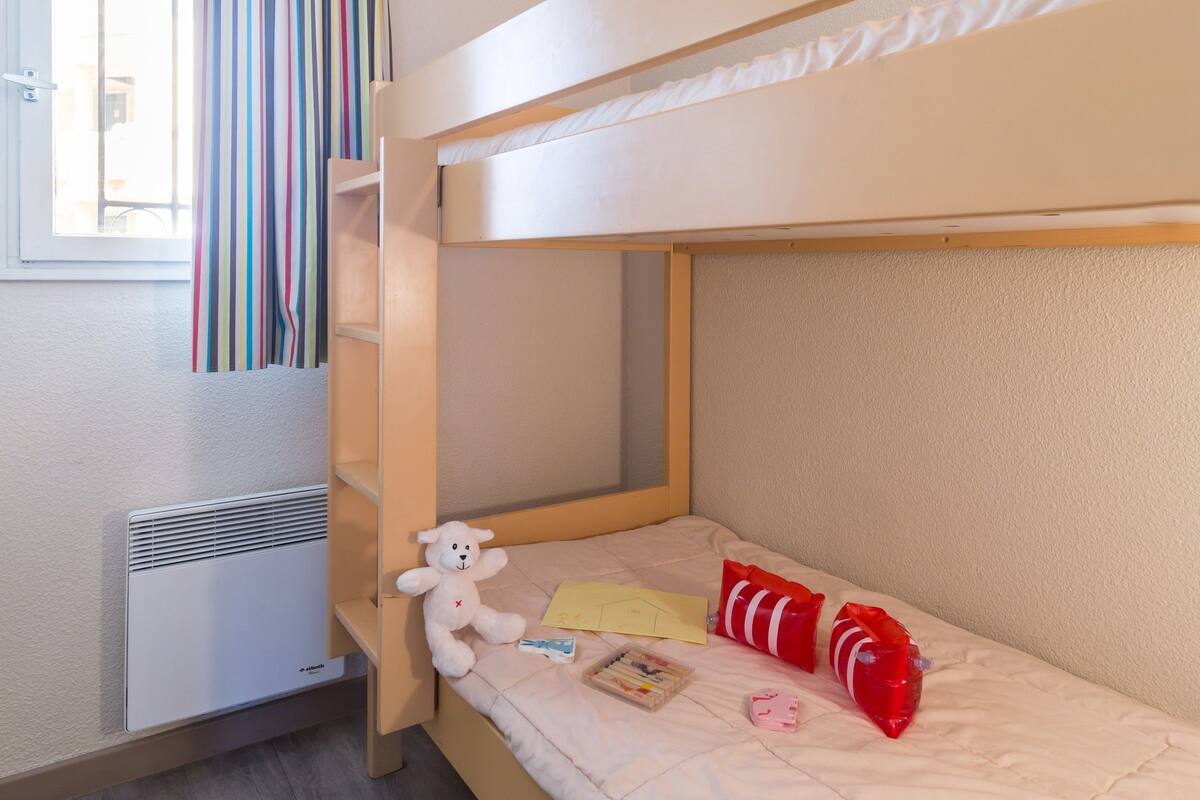 Een slaapkamer met een stapelbed, een raam en een teddybeer.