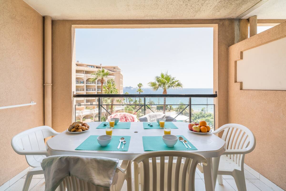 Een balkon met een ontbijttafel, inclusief kommen, lepels en een schaal met fruit.