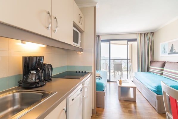 Cocina compacta con cafetera, microondas y lavavajillas. Se ve un balcón con vistas a través de una puerta abierta.