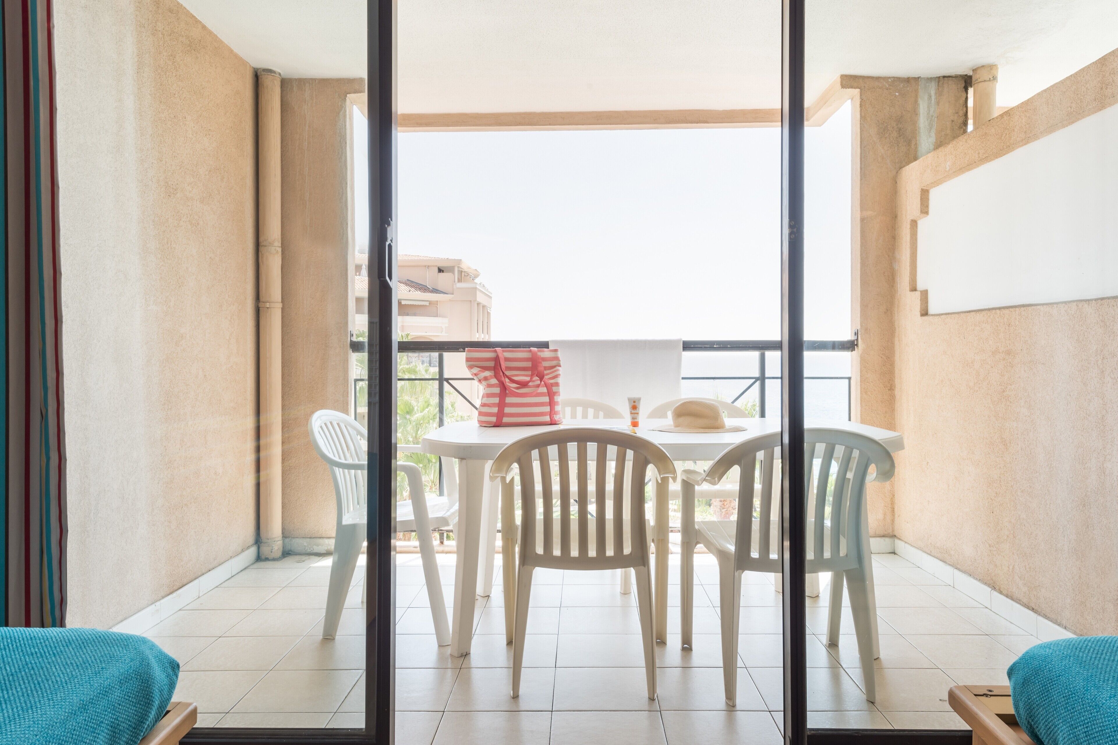 Un balcon avec une table et des chaises, un sac à rayures et une bouteille.