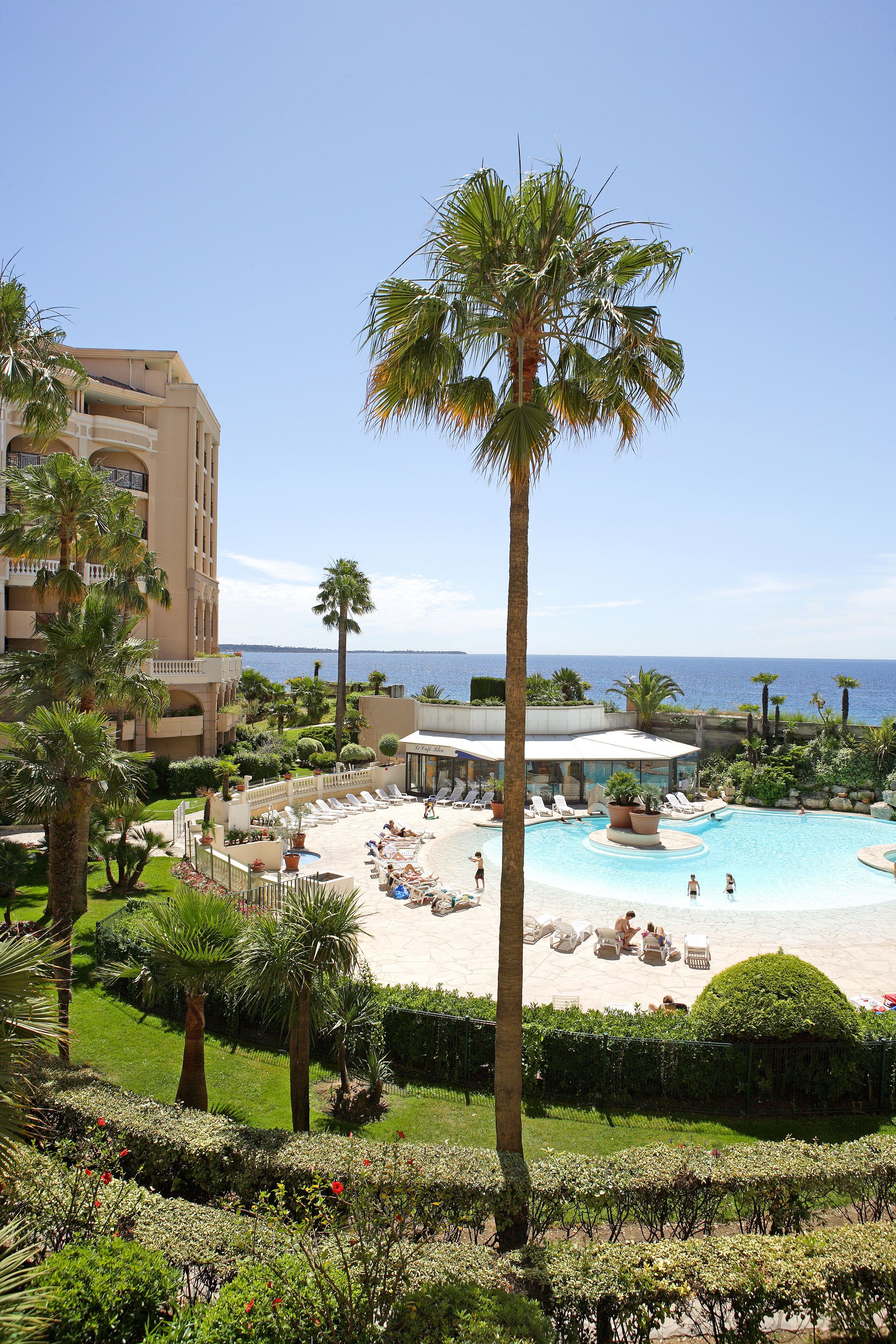 A resort with a pool, palm trees, and a view of the sea.