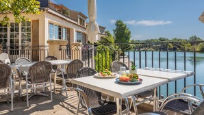 An outdoor dining area with a table and chairs, a view of a body of water, and a building in the background.