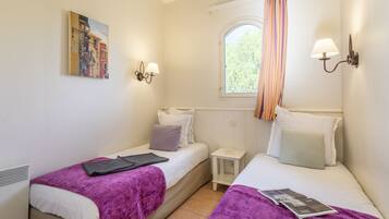 Un dormitorio con dos camas, una ventana con cortinas, una mesita de noche pequeña y lámparas de pared.