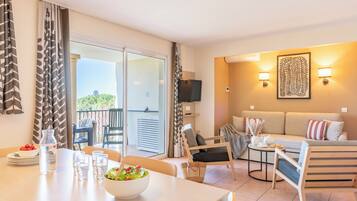 A hotel room with a dining area, a sofa, a TV, and a balcony with a view.