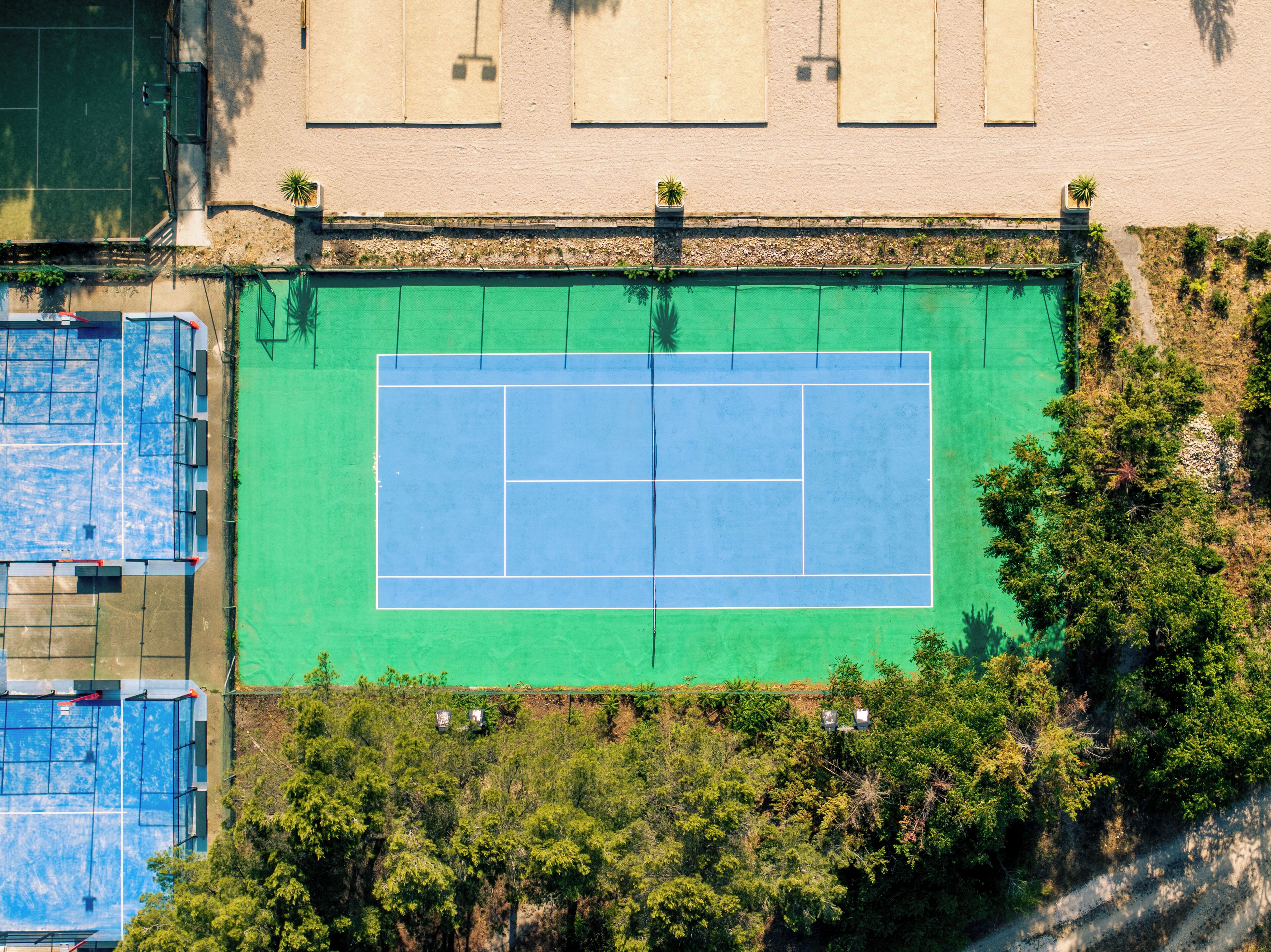 An aerial view of a tennis court surrounded by trees and a building with windows.