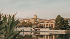 A waterfront property with a central building featuring a tower, surrounded by trees and a calm lake.
