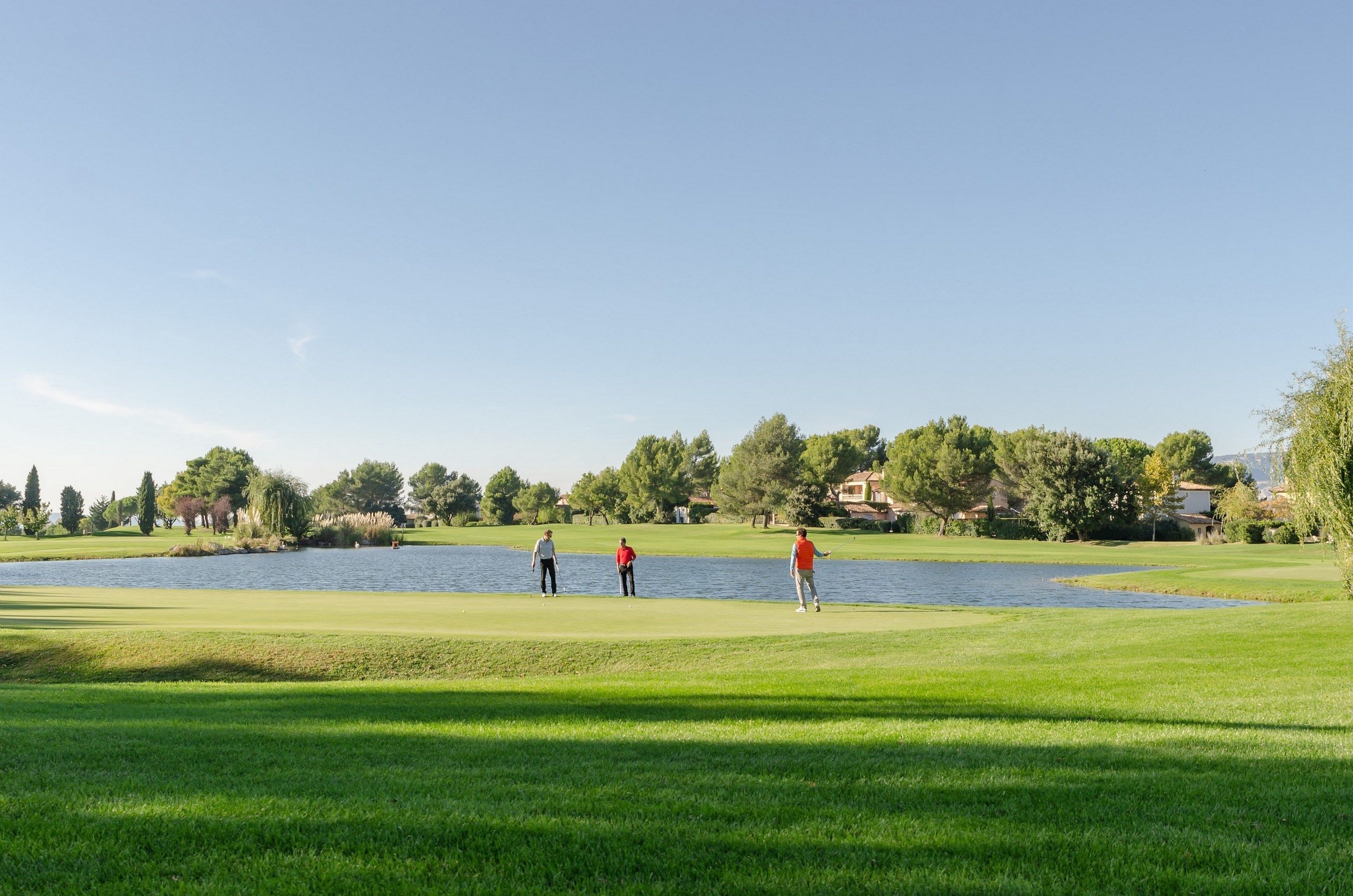 A golf course with a lake, trees, and houses in the background.