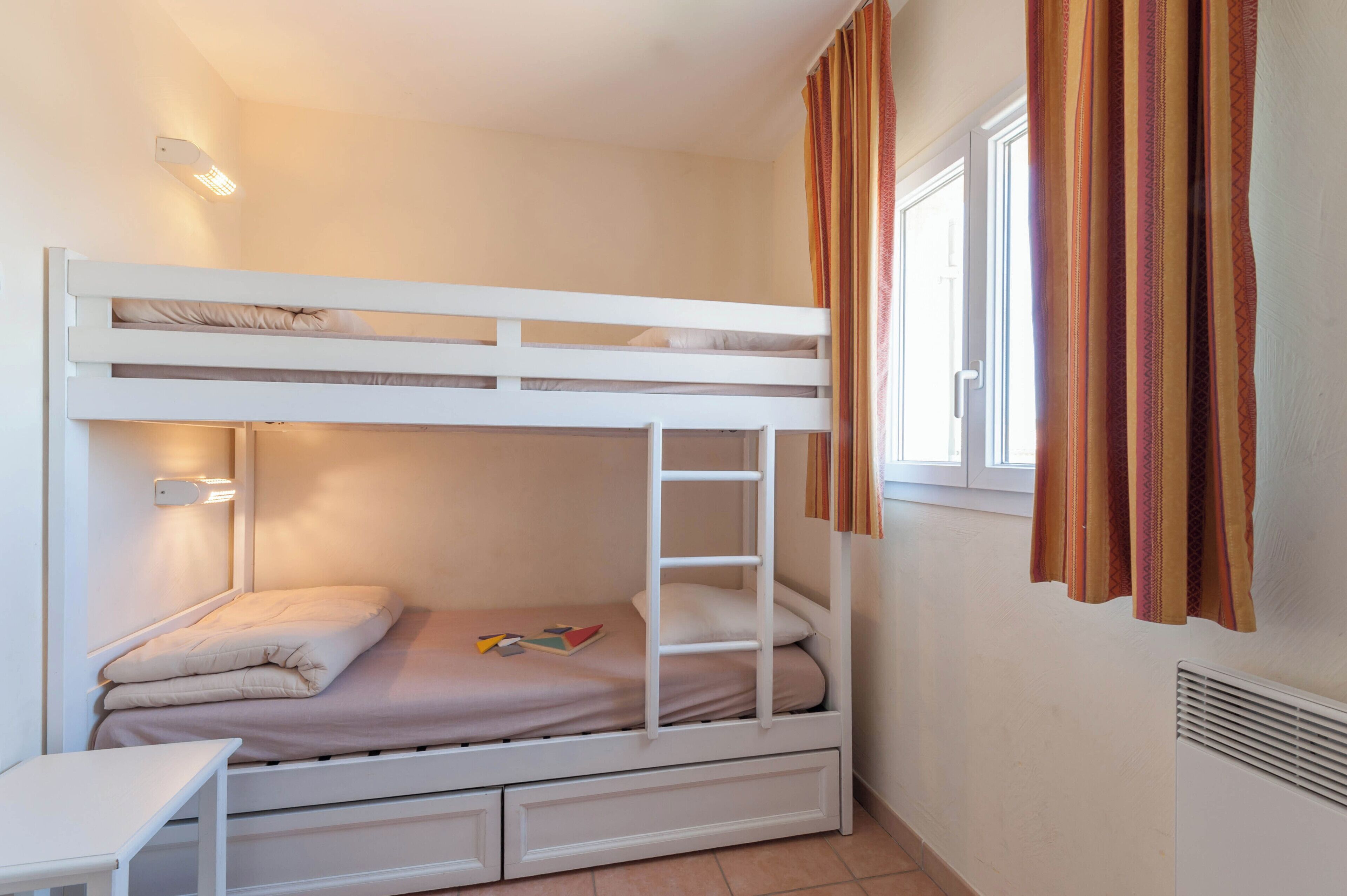 A bunk bed with a ladder, a bedside table, and a window with curtains.