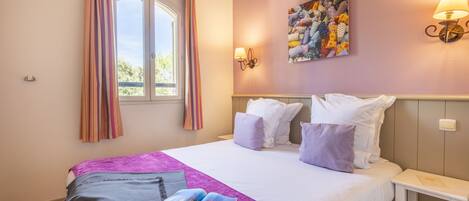 A bedroom with a bed, pillows, a bedside table, a window with curtains, and wall art.