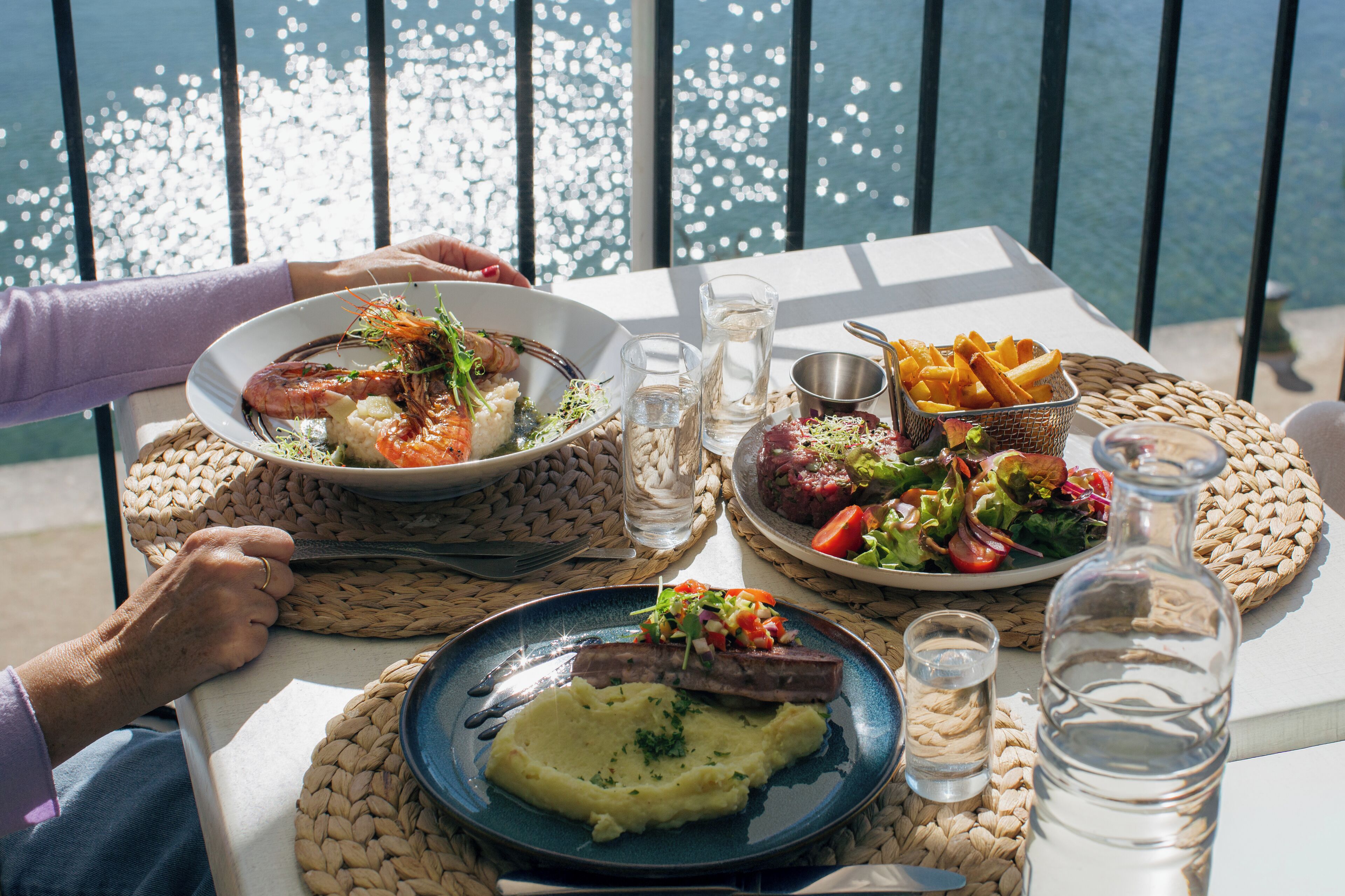 Una mesa dispuesta con platos de comida, una botella de agua y vista al agua.