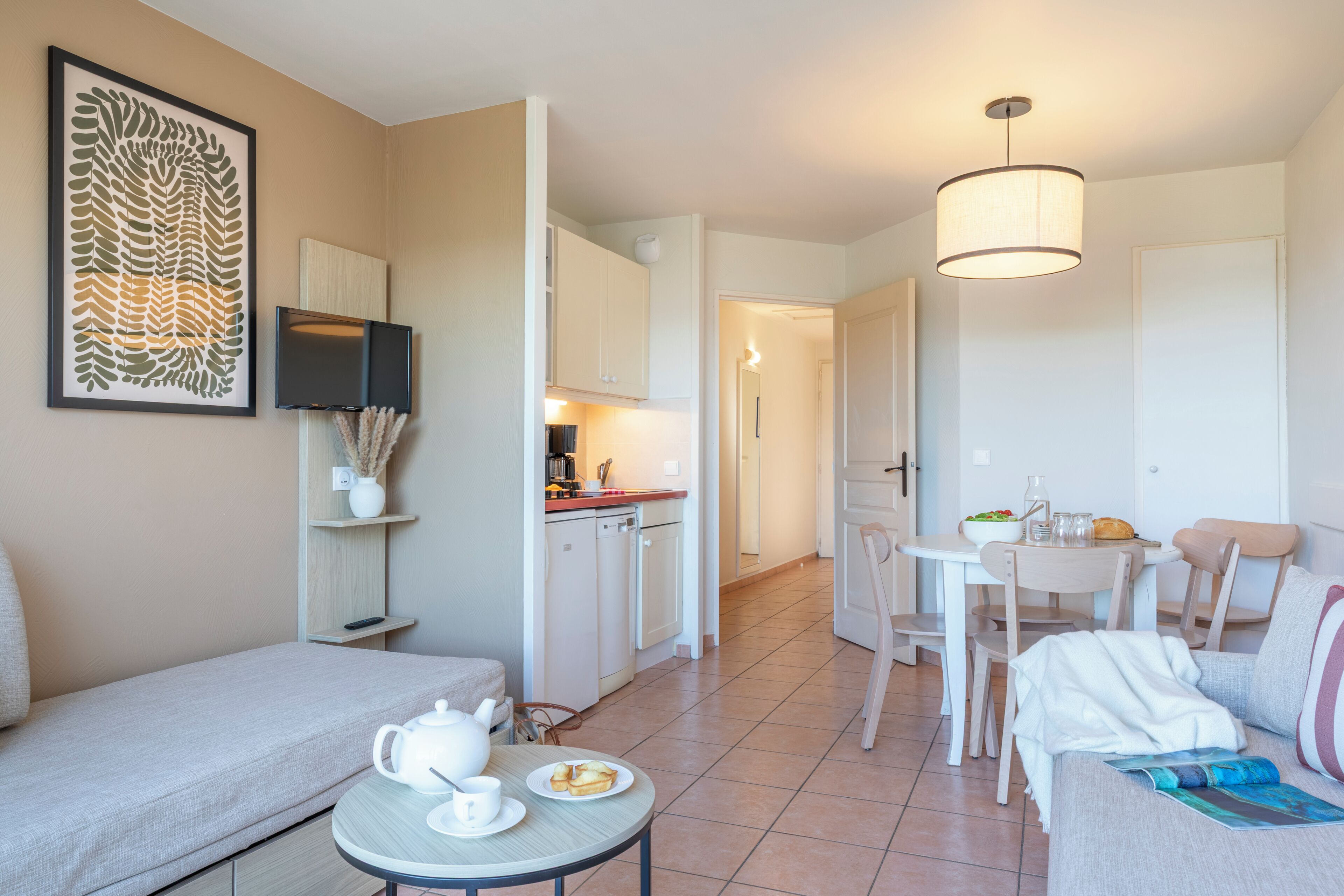 Una sala de estar moderna con un sofá, una mesa de comedor, una zona de cocina y un televisor montado en la pared.