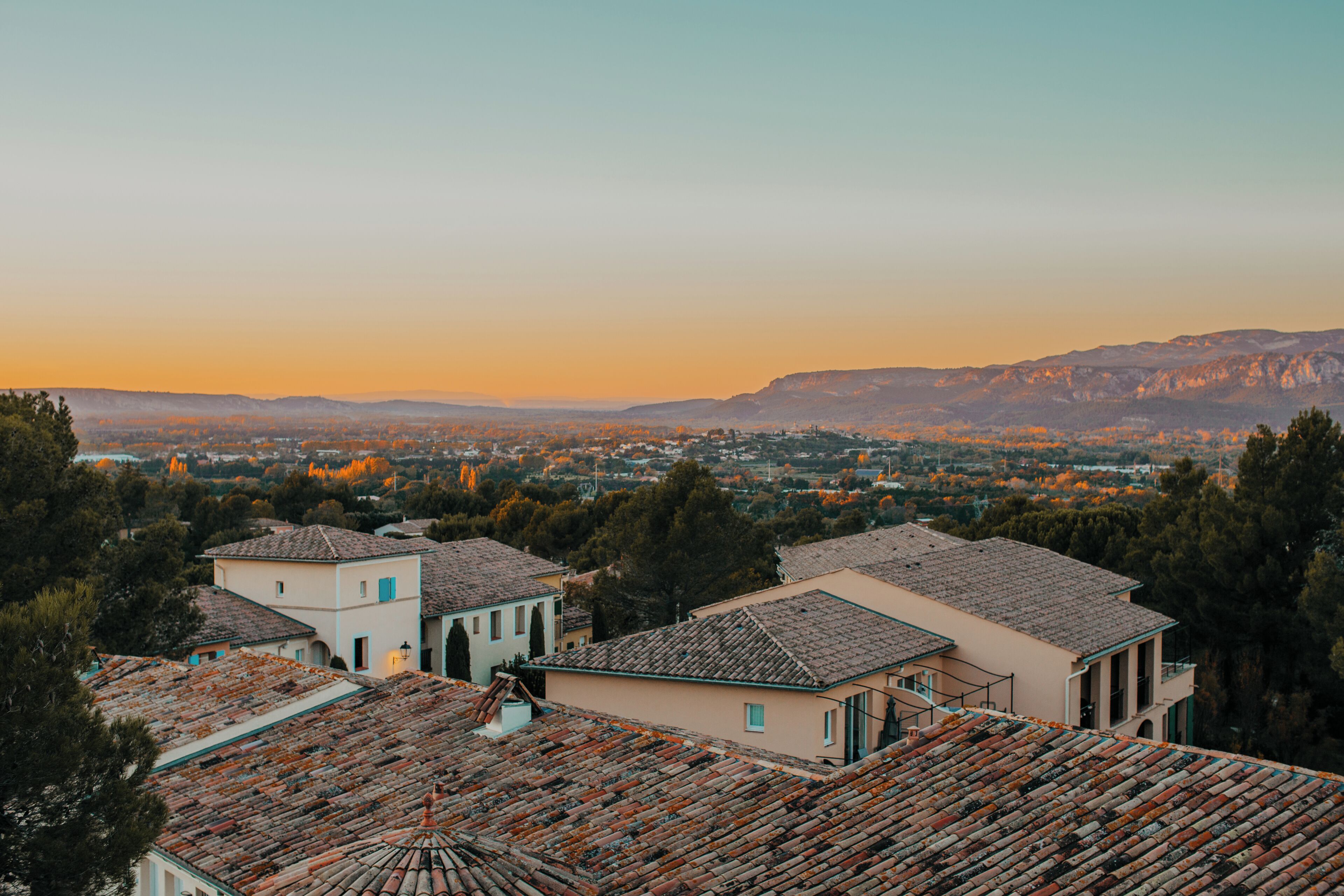 A residential area with terracotta-tiled roofs, a mix of single and multi-story buildings, and a mountainous backdrop.