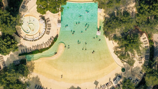 An aerial view of a resort with a large pool, sun loungers, and a circular water feature.