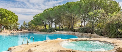 A swimming pool with a hot tub, surrounded by trees and stone structures.