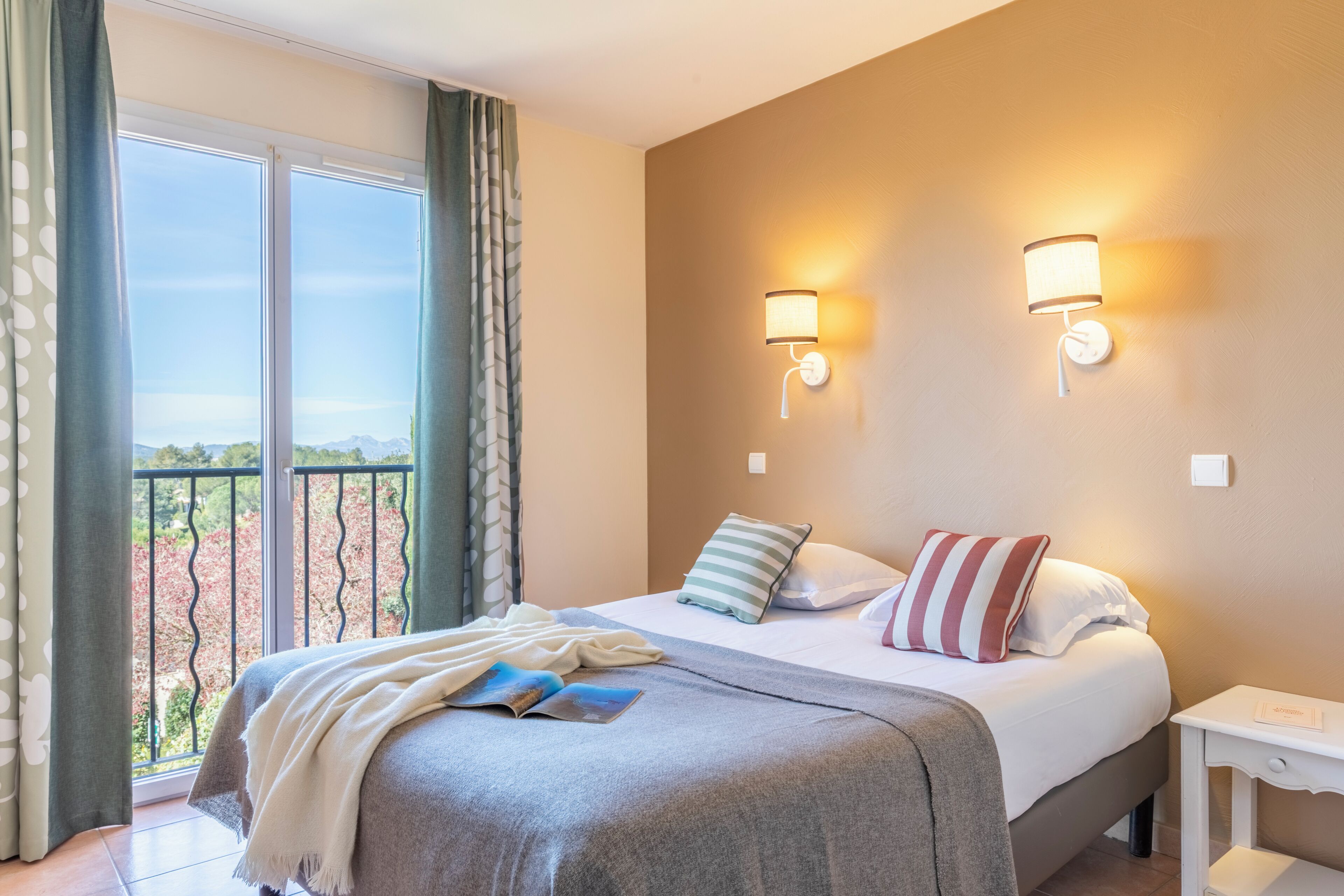 Habitación de hotel con cama, dos lámparas de noche, mesita de noche y vistas al exterior.