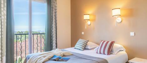 Habitación de hotel con cama, dos lámparas de noche, mesita de noche y vistas al exterior.