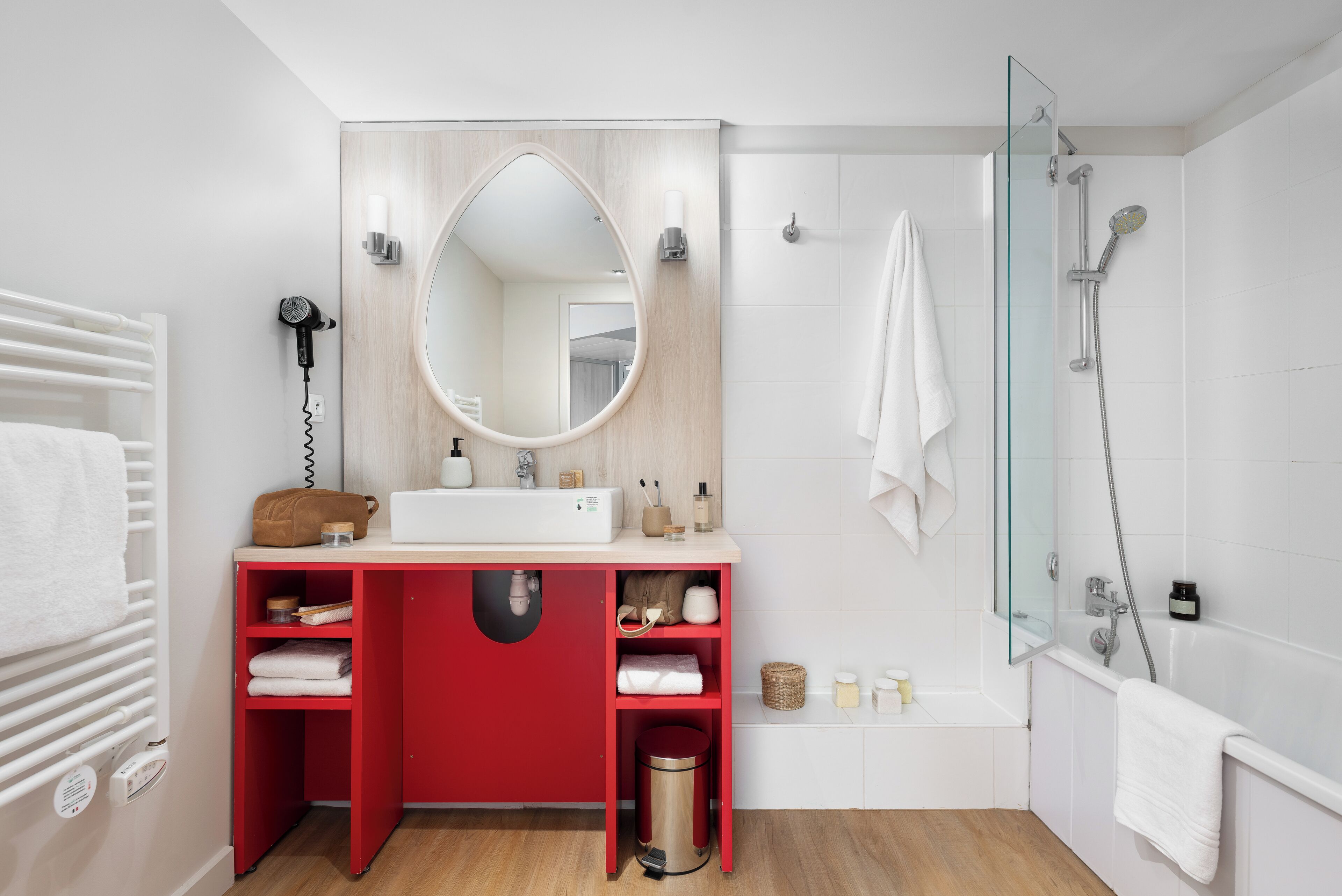 A modern bathroom with a red vanity, a large mirror, a glass shower enclosure, and a white bathtub.