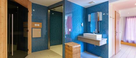 A modern bathroom with blue-tiled walls, a wooden door, a white sink, and a wicker basket.