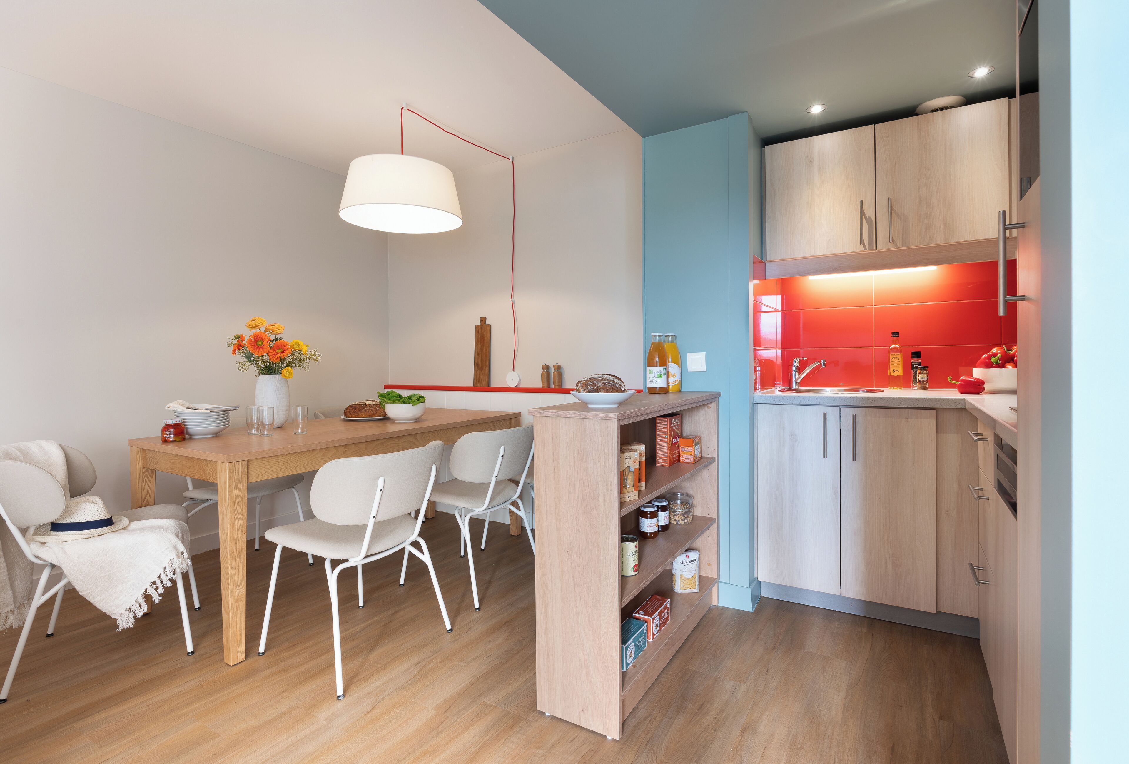 Eine moderne Küche mit Holzausstattung, ein Essbereich mit weißen Stühlen und einer roten Akzentwand.