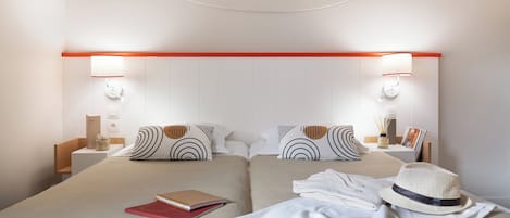 A double bed with a headboard, two bedside tables, a nightstand, a red book, a white hat, and a white blanket.