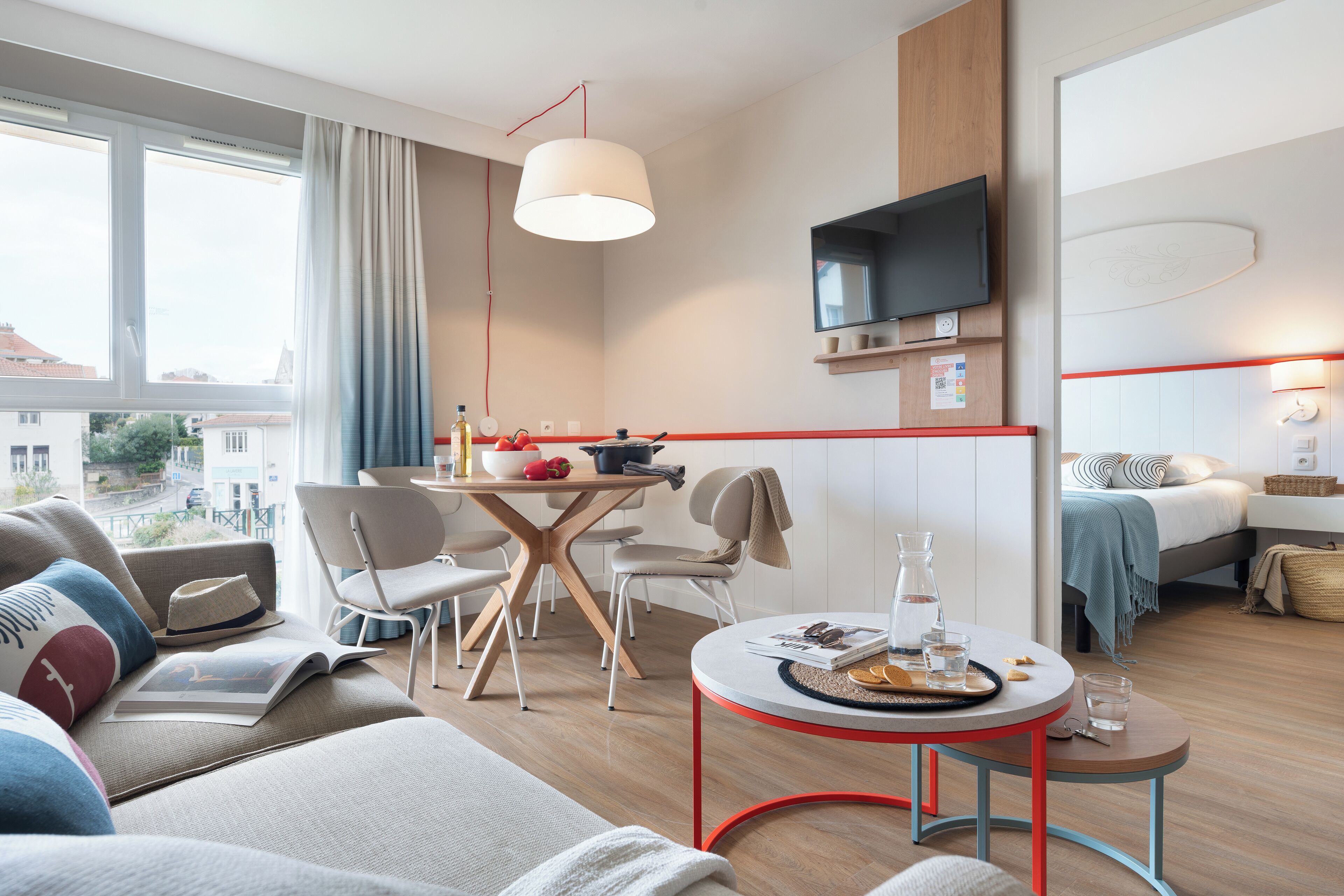 A modern hotel room with a dining area, a sofa, a TV, and a bed.