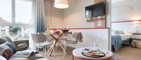 A modern hotel room with a dining area, a sofa, a TV, and a bed.
