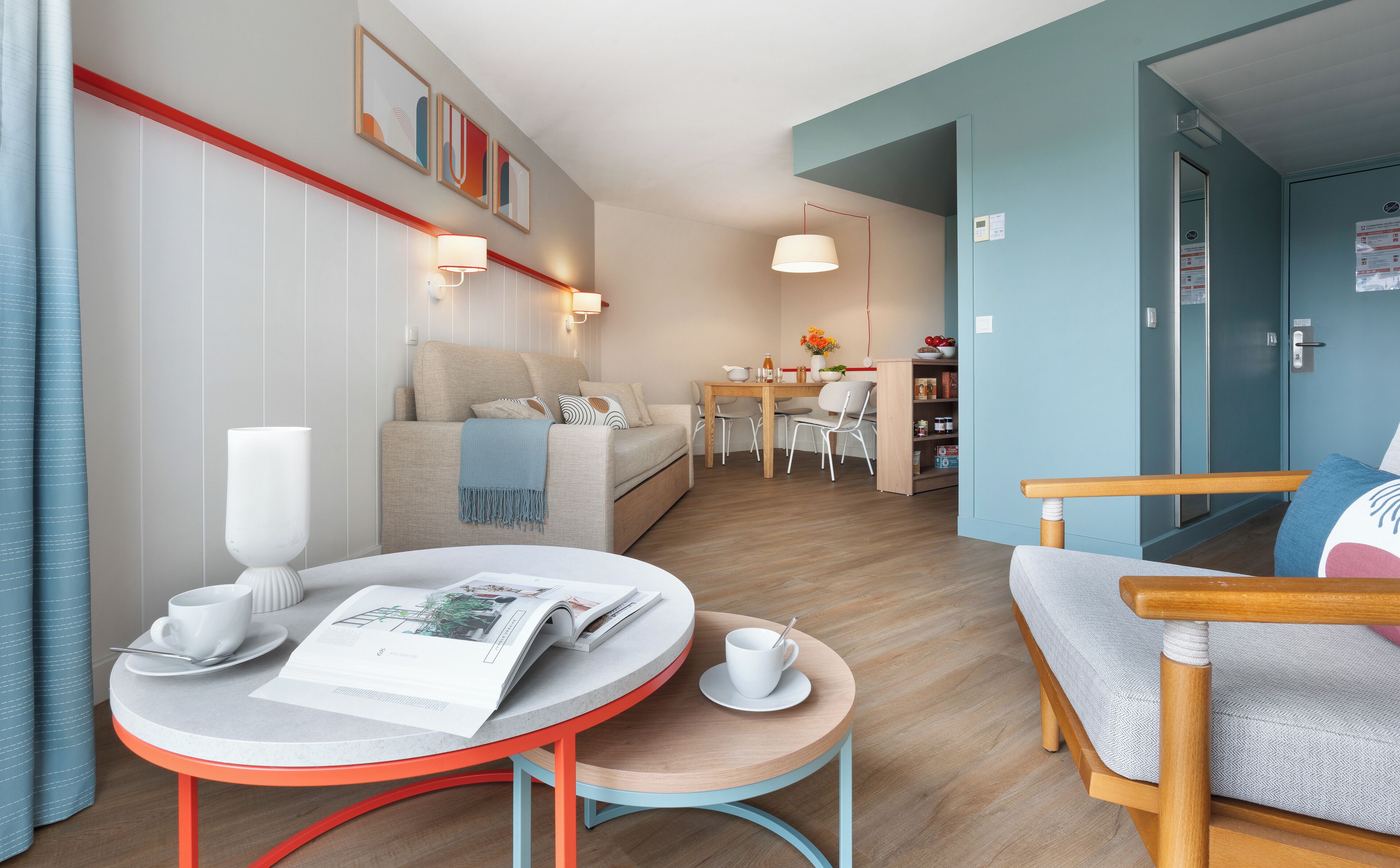 Een moderne hotelkamer met een bank, een eettafel en een klein rond tafeltje met een tijdschrift en een kop.