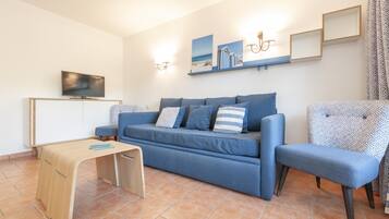 A living room with a blue sofa, a wooden coffee table, a TV on a cabinet, and wall-mounted lights.