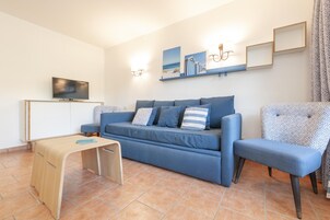 A living room with a blue sofa, a wooden coffee table, a TV on a cabinet, and wall-mounted lights.